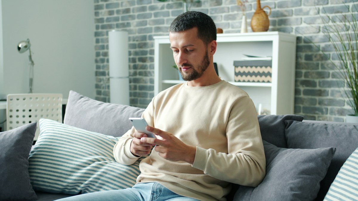 Man relaxing on the sofa and updating his dating profile on his phone